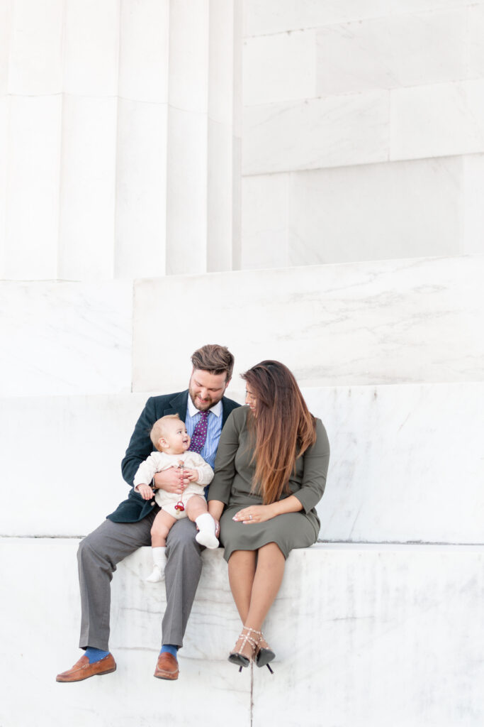 family of three sits on the steps of the Lincoln Memorial in Washington D.C.