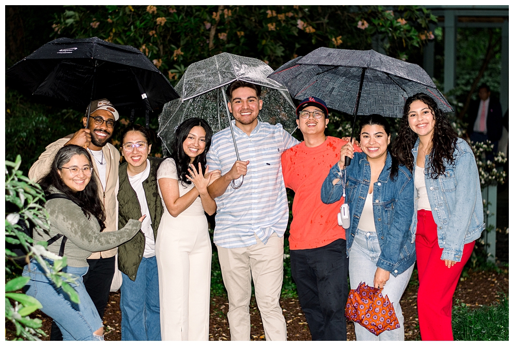 A group of friends stand with a recently engaged couple after a surprise proposal at McCrillis Gardens in Bethesda, Maryland.