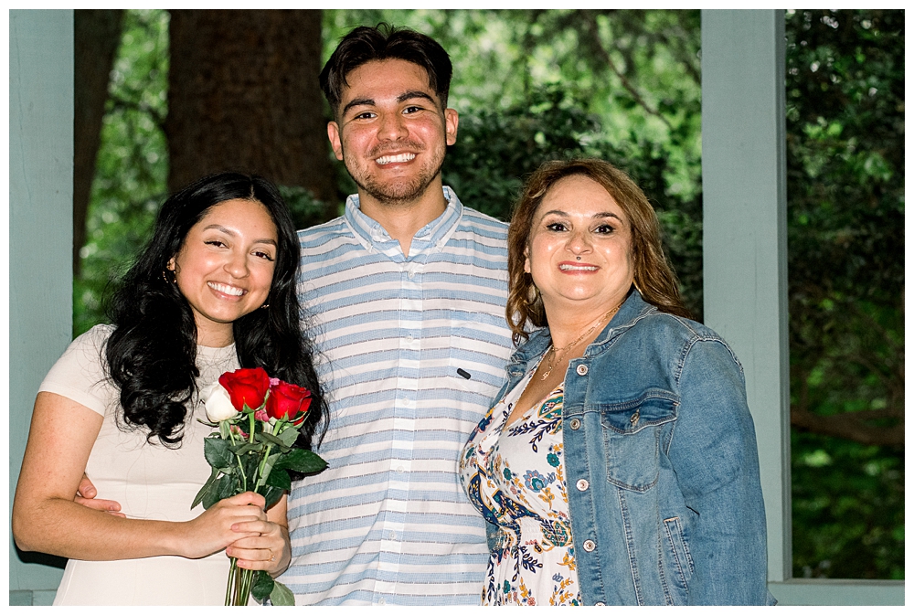 A recently engaged couple stands with a family member after a surprise proposal at McCrillis Gardens in Bethesda, Maryland.