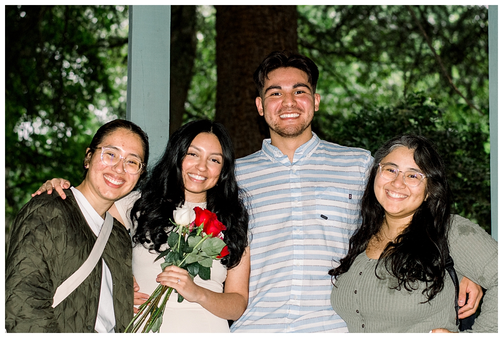 A group of friends stand with a recently engaged couple after a surprise proposal at McCrillis Gardens in Bethesda, Maryland.