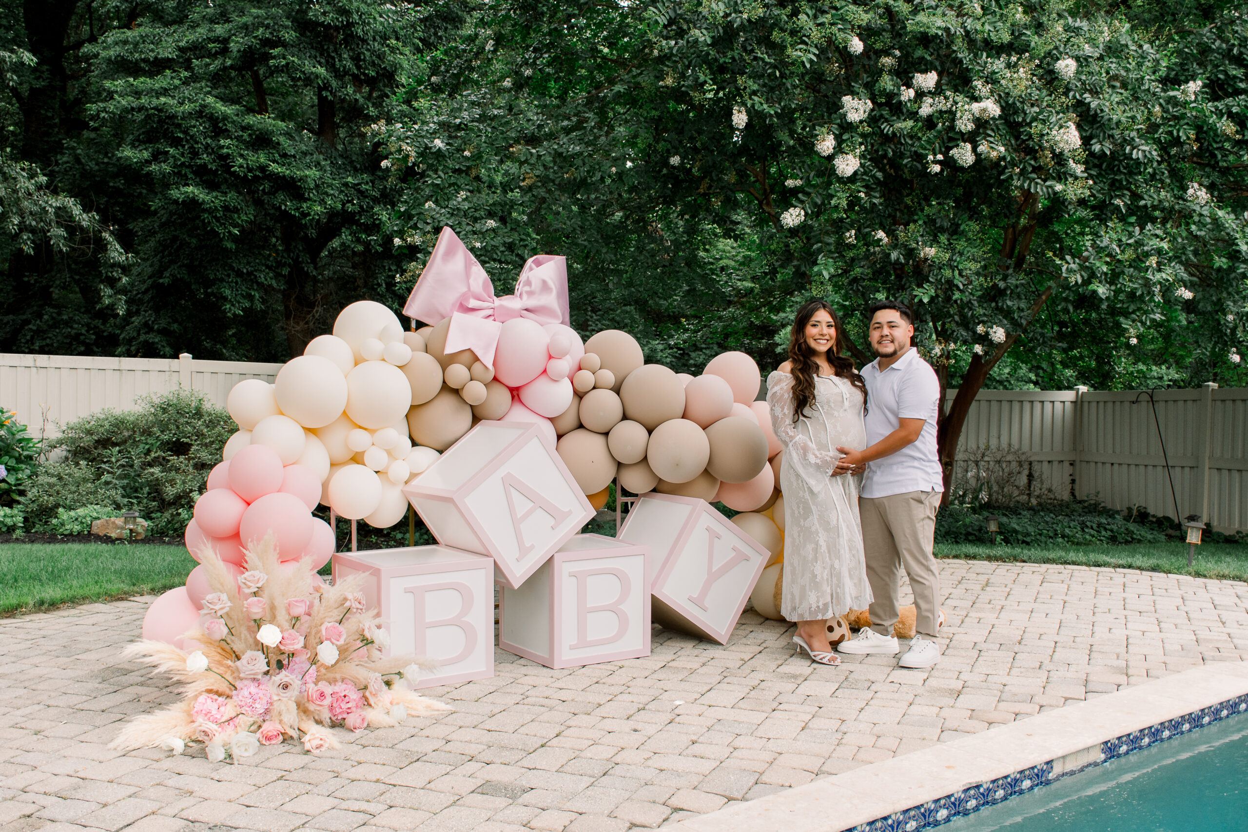 An pregnant woman and her partner stand together by a large "BABY" balloon arch at their luxury baby shower for baby girl Rosemary in Maryland.
